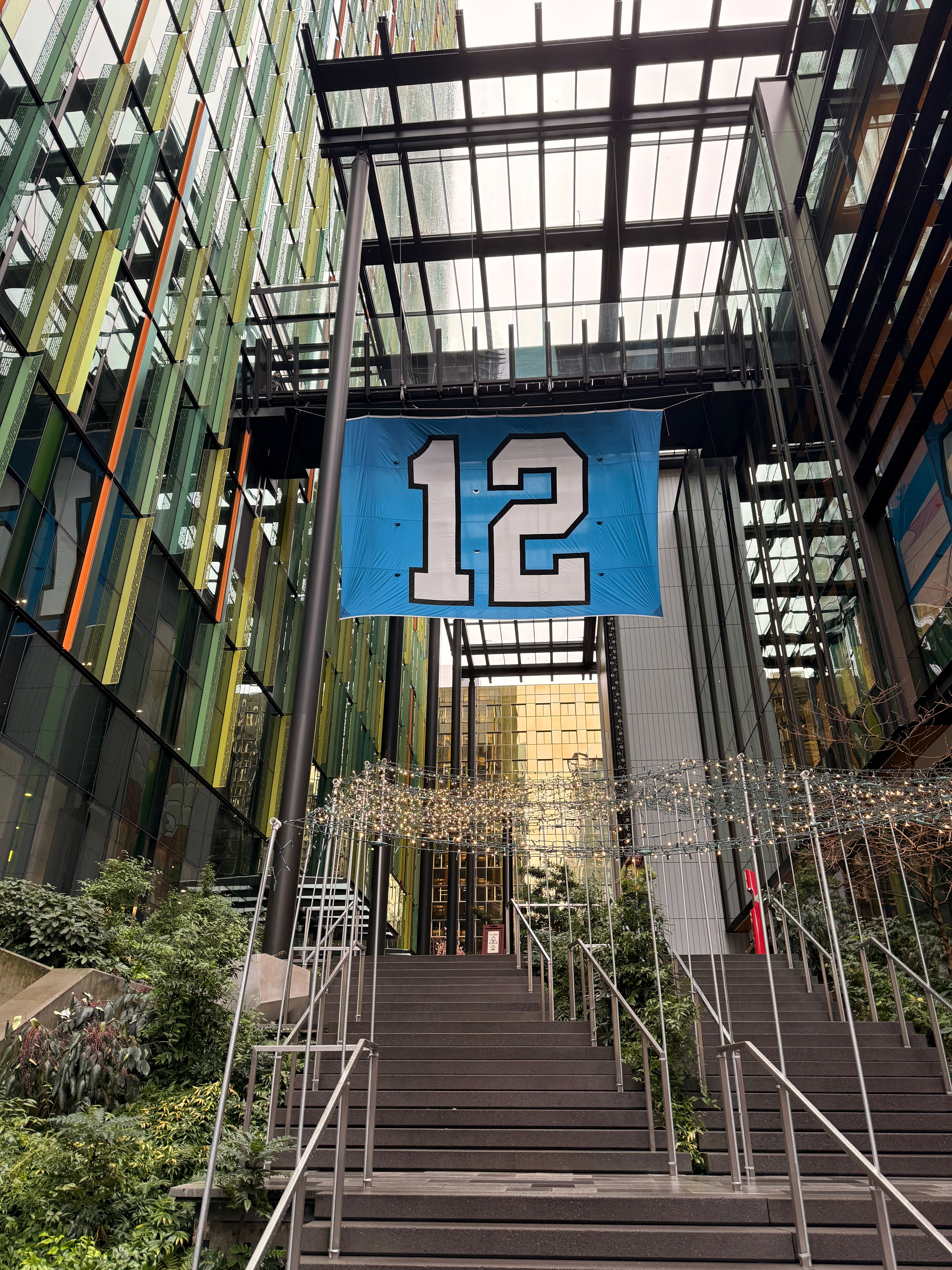 A giant 12 flag hanging between modern glass buildings in downtown Seattle