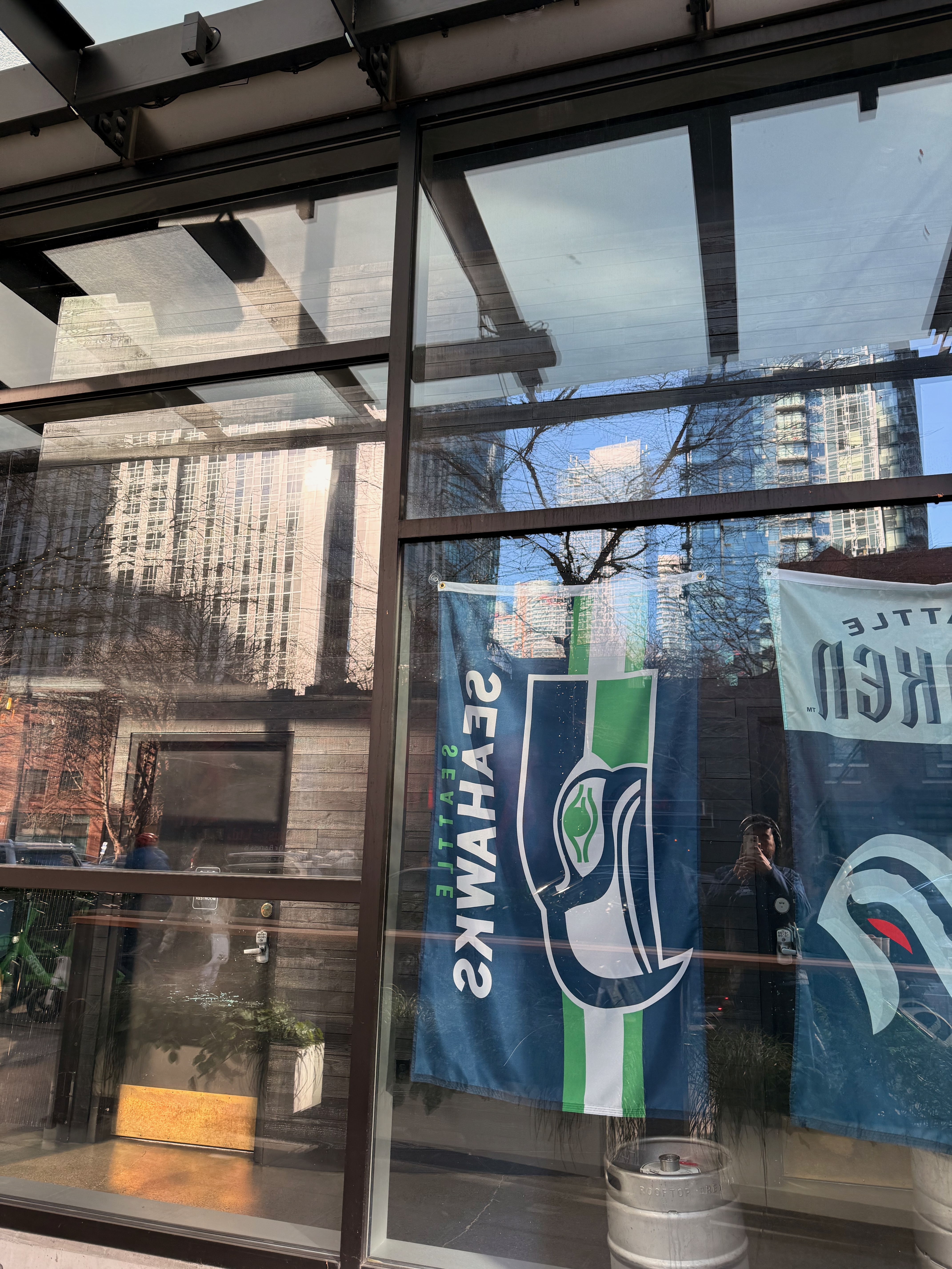 Seahawks and Kraken flags displayed in a storefront window reflecting the city
