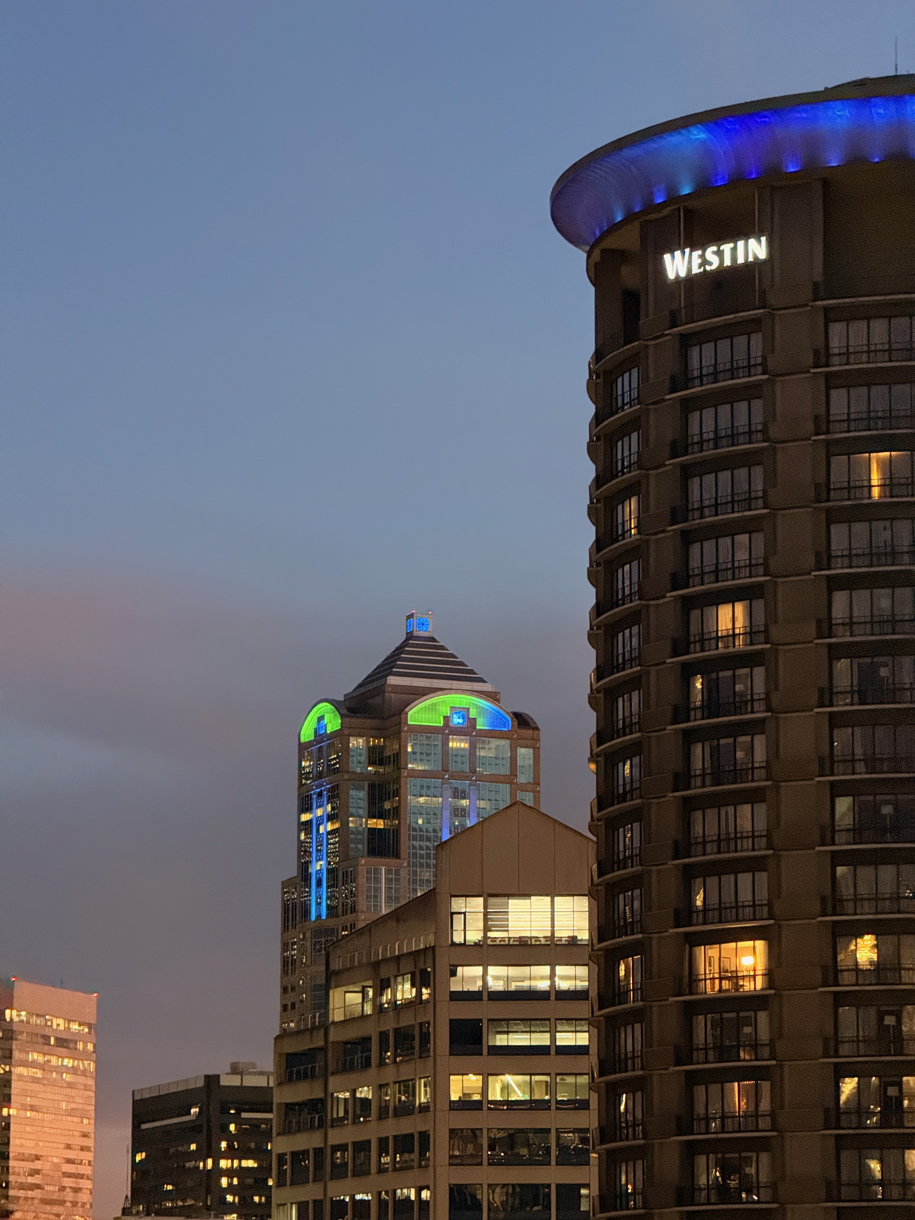 Seattle skyline at dusk with buildings lit in blue and green near the Westin