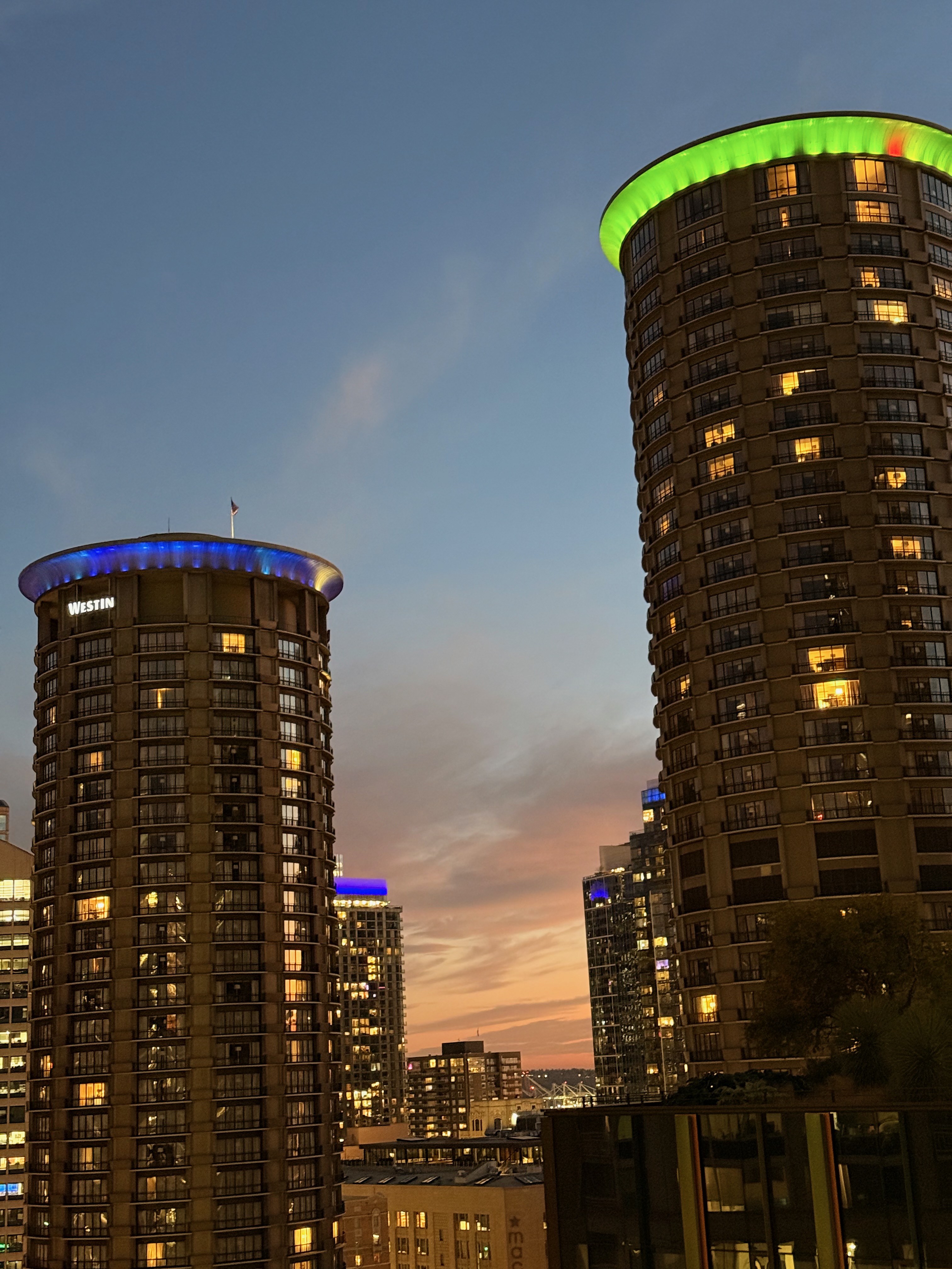 The Westin towers lit up in blue and green against a sunset sky